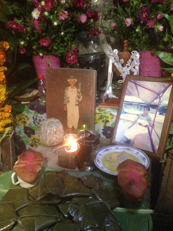 Tamales, cups of atole, pollo de pipian, and pan de muerto accompany the photos of deceased relatives on the altar.